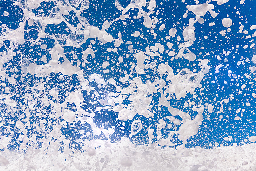 Water drops and white sea foam splashing in the air against a blue sky and forming a beautiful abstract motion pattern