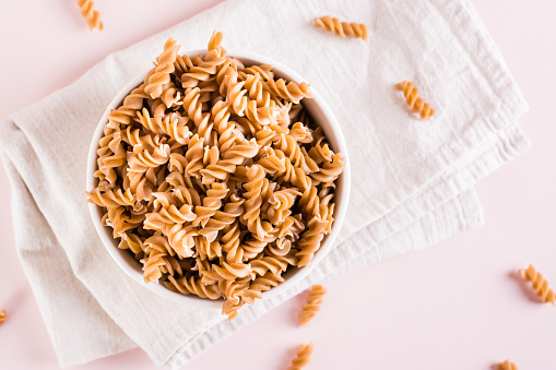Raw pasta from buckwheat flour in a bowl and groats in a bowl on a pink background. Top view. Closeup