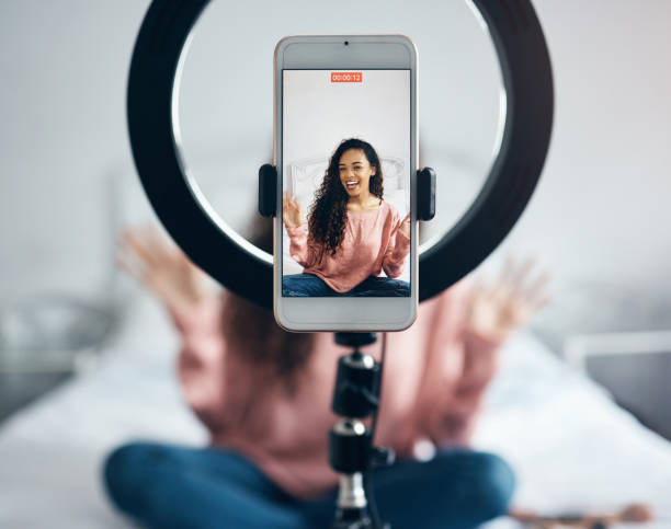 transmissão ao vivo, telefone e mulher negra falando em podcast de vídeo no quarto de sua casa. menina feliz e animada ou influenciadora falando na internet ou mídia social com um celular e luz de anel - mobile phone home video camera video photograph - fotografias e filmes do acervo