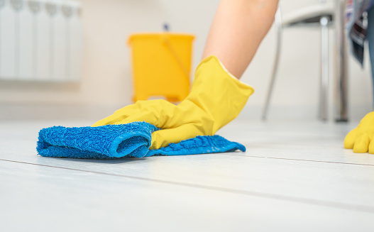 Deep Cleaning service. Professional cleaner washing white floor in living room of apartment. female hands in gloves wipe white floor with text cleaning. Cleaning service concept