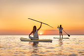 Two happy girls walks at sunset lake on sup boards