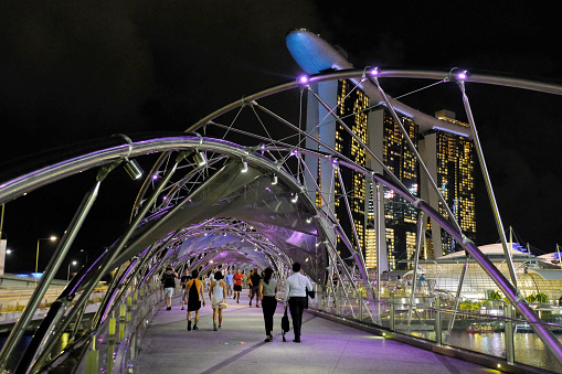 People walking on the Helix Bridge, a pedestrian bridge linking Marina Centre with Marina South in the Marina Bay area in Singapore. In the distance, the Marina Bay Sands.