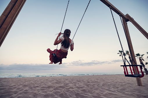 Teenage girl having fun swinging at the beach playground. Summer day evening \nCanon R5