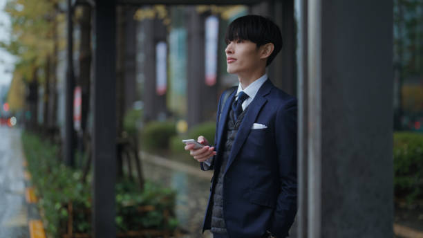 A businessman is sheltering from rain and waiting where he can avoid getting wet in the city.