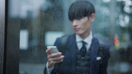 A businessman is sheltering from rain and waiting where he can avoid getting wet in the city.