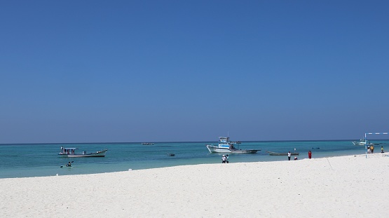 A white beach above the blue ocean with sailing boats under the blue sky in Lakshadweep island, India