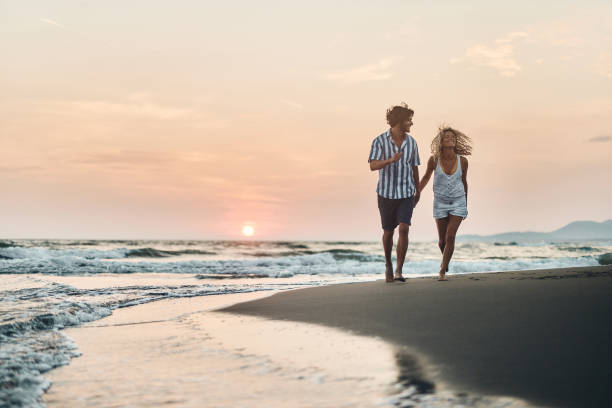 Young happy couple running on the beach at sunset.