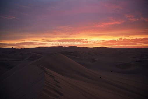 A scenic shot of a sunset over sandy dunes in Huacachina, Peru