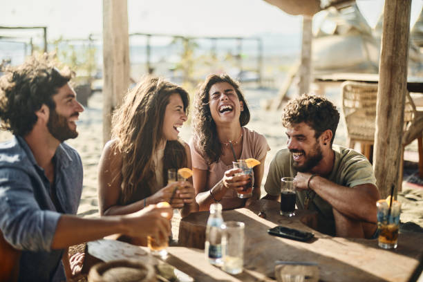 Cheerful couples talking in summer day at a beach bar. Group of cheerful friends communicating while spending a summer day in a beach café. beach bar stock pictures, royalty-free photos & images