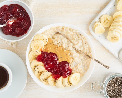 A top view of oatmeal porridge with strawberry jam, peanut butter, banana, and chia