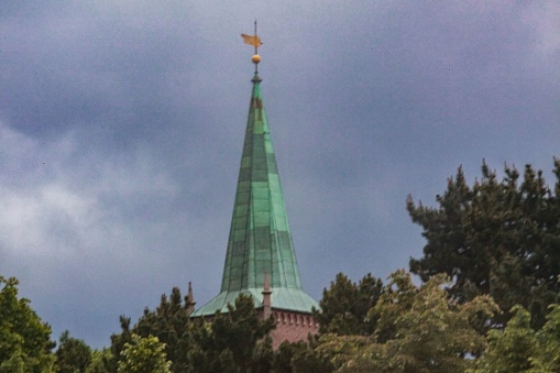 A blurry shot of a tower rooftop surrounded by trees in the cloudy sky.