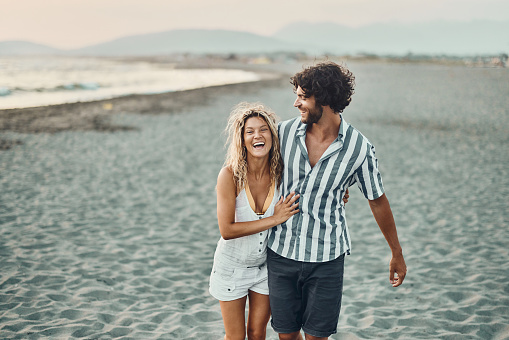 Young cheerful couple having fun while taking a summer walk on the beach. Copy space.