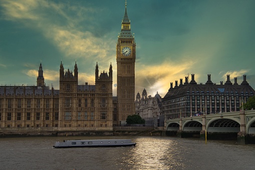 A scenic view of the Palace of Westminster on the bank of the river Thames with gorgeous London bridge at sunset