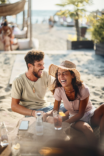 Young cheerful couple talking about something funny while spending a summer day in a beach café.