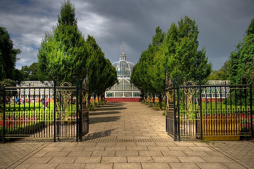 A scenic view of a glasshouse in Queen's Park in Glasgow, Scotland with green trees on a gloomy day
