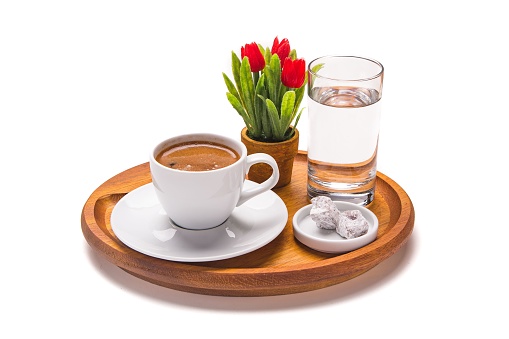 An isolated shot of a cup of coffee with water, treats, and small flowers on a wooden tray