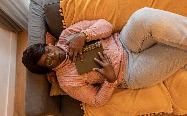 Top view of sleeping African American senior woman on the sofa with a book