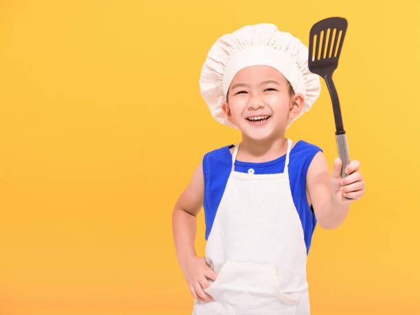 istock Happy little boy in chef uniform on yellow background 1446841580