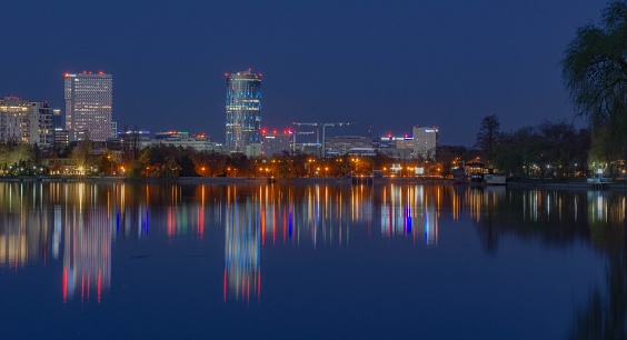 A panoramic view of a lake reflecting lights of buildings at Herastrau Park in Bucharest, Romania at night