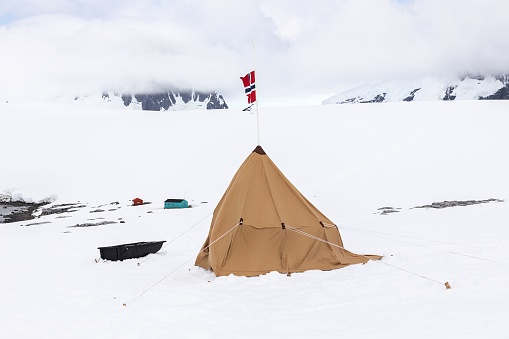 The Norwegian flag waving on top of a camping tent in Antarctica on a glacier against snowy mountains
