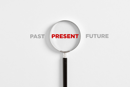 Focusing on the current situation, positive thinking and mindset concept. Magnifying glass on the word present with the words past and future.