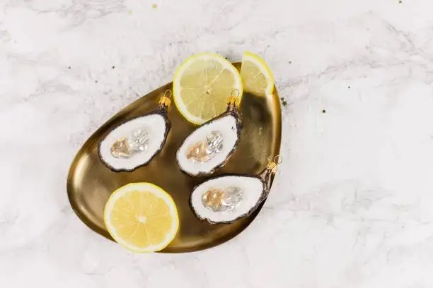 Lemon slices and oysters are decorated in a golden bowl. Everything is laid on a marble background and it is decorated with glitter.