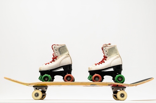 Two white rollerskates with colorful wheels on a skateboard on white background