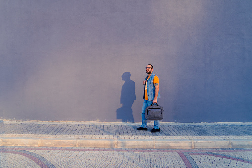 Young man returning home from work with laptop bag and casual jeans clothes at sunset.