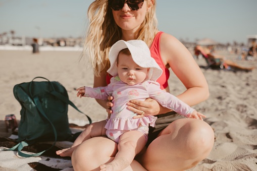 A closeup shot of a mother and a baby playing in sand on the beach