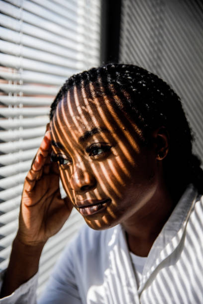 istock Female scientist standing by the window, blind shades playing on her face while she takes a break from work 1446848461