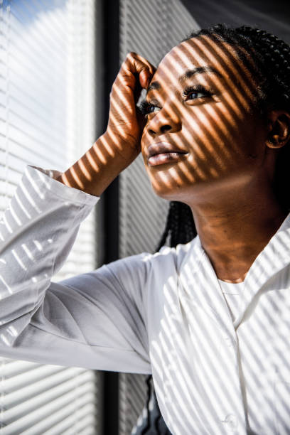 istock Female scientist standing by the window, blind shades playing on her face while she takes a break from work 1446848464