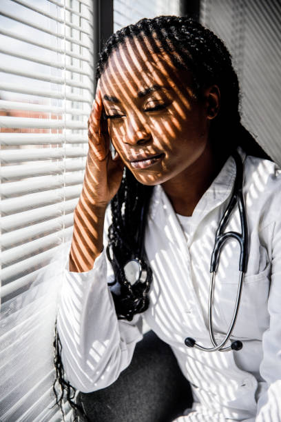 istock Female scientist standing by the window, blind shades playing on her face while she takes a break from work 1446848468