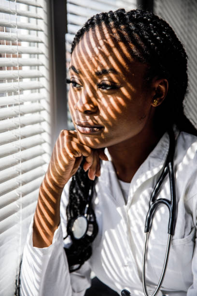 istock Female scientist standing by the window, blind shades playing on her face while she takes a break from work 1446848469