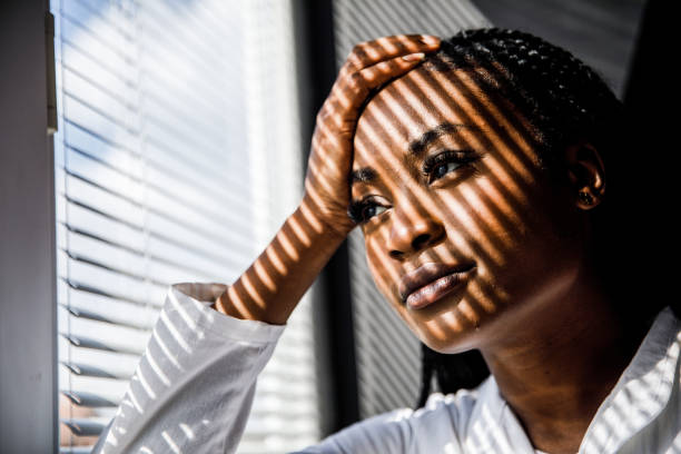 istock Female scientist standing by the window, blind shades playing on her face while she takes a break from work 1446848481