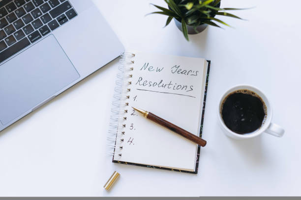 istock open notepad with new year resolutions and empty list. Flower, laptop and coffee cup on background. 1446848608