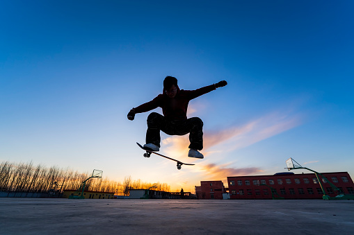 In the evening, a boy is playing skateboard. The silhouette of a boy on a skateboard