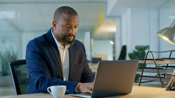 istock Laptop networking, planning and black man with coffee, digital finance and typing email on internet at work. Accounting business, strategy and African businessman with a pc for financial information 1446850940