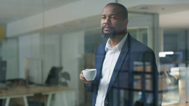 istock Coffee, corporate and thinking black man at work, professional business and executive idea at a window. Office tea, company focus and African businessman working with  drink in the workplace 1446854497