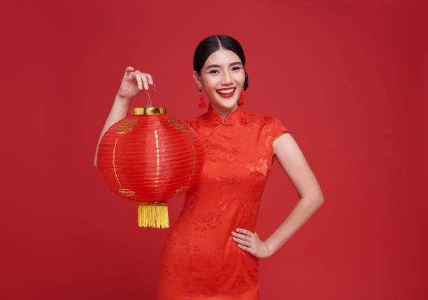 Happy Chinese new year. Asian woman wearing traditional cheongsam qipao dress holding Chinese lanterns isolated on red background. stock photo