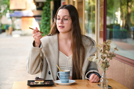 Young woman eating a cake and drinking coffee in a cafeteria.