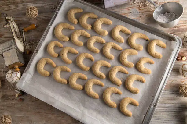 Fresh and homemade baked vanilla crescents or vanillekipferl. Traditional german or austrian christmas cookies. Served warm on a baking tray on wooden table with old fashioned kitchen utensils. Flat lay