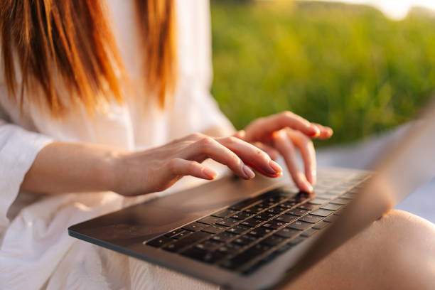 istock Close-up cropped shot of unrecognizable female freelancer working typing on laptop computer sitting on beautiful field with green grass. 1446862134