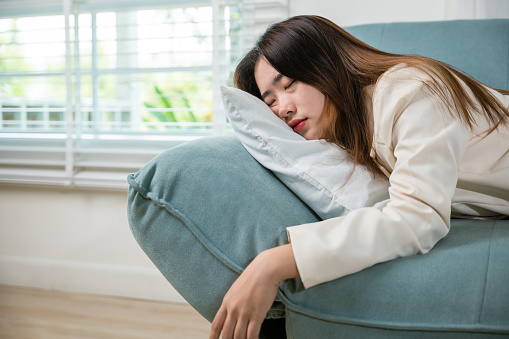 Tired woman sleeping closed eyes on sofa in living room at home after overworked working, Asian female resting falling asleep lying on couch, Close up face