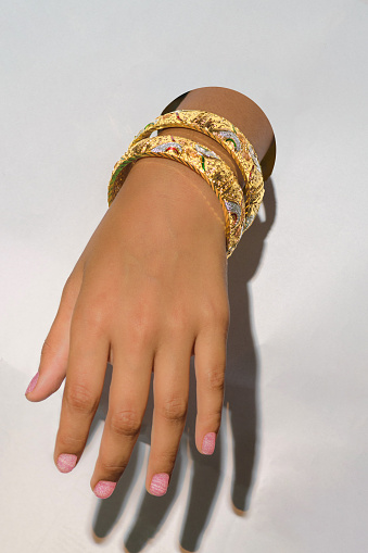 Closeup female hand with golden bangles on a white background. Beauty pink nail polish applied.