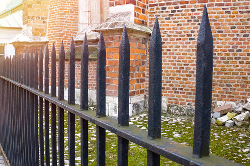 A metallic fence is in a prospect, on a background old brick building in a sunny day.