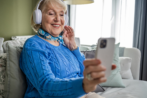 Smiling senior woman sitting on the sofa, using a mobile phone and laughing