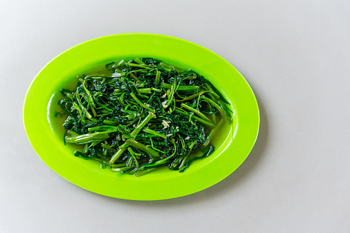 stir fried water spinach vegetable with garlic (Indonesian : Tumis Kangkung Bawang Putih) Served on green plate isolated on gray background.