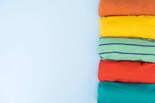 close up of rolled colorful t shirt clothes on blue table background, travel concept