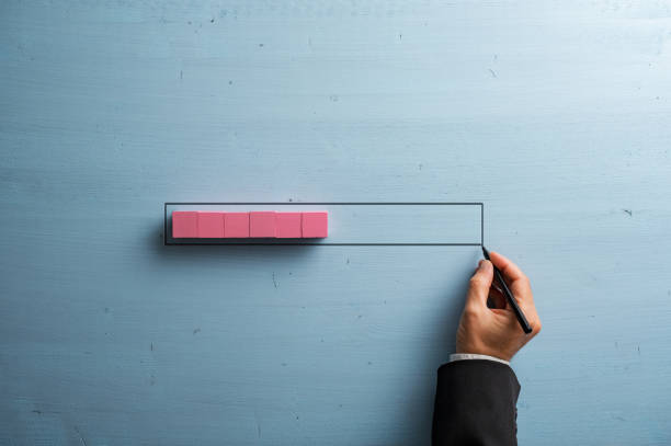 istock Male hand drawing a loading bar with pink wooden blocks representing the progress 1446873250