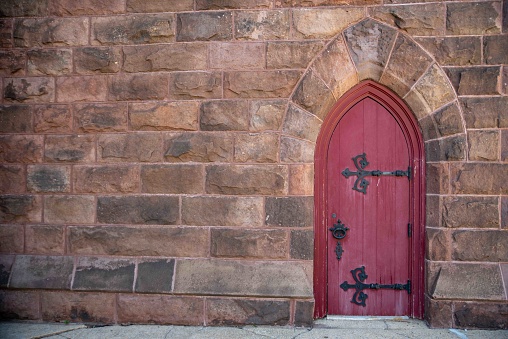 No people, and copy space in this image3 of a red church door with decorative hinges and door knob with stone arch and colorful stone wall.